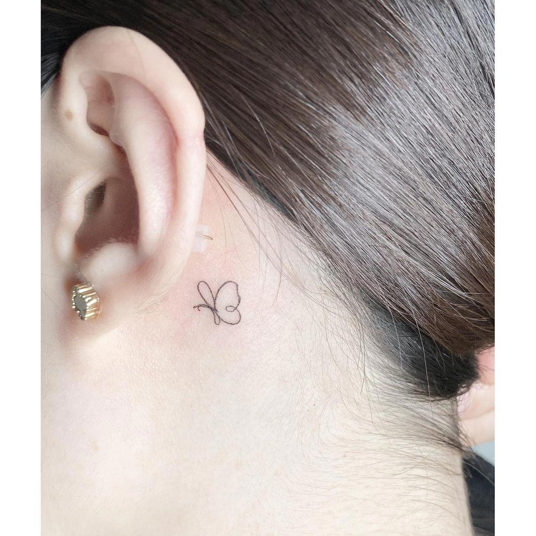 Silueta de mariposa tatuada tras la oreja